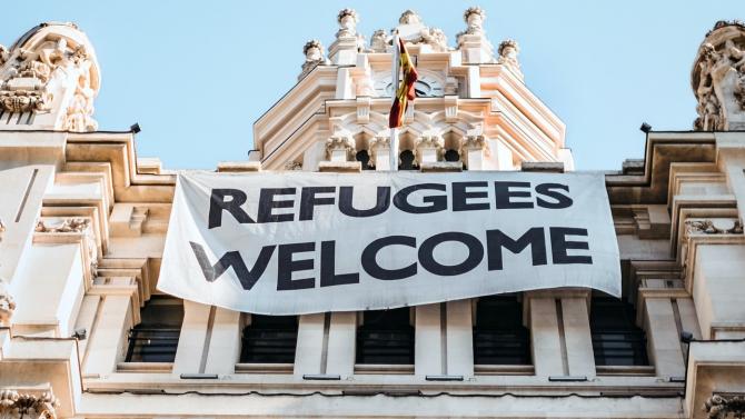 large public institutional building with large sign reading "refugees welcome" draped across its front