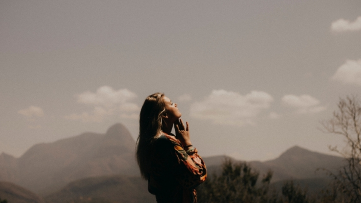 A woman meditating outside with mountains in the background