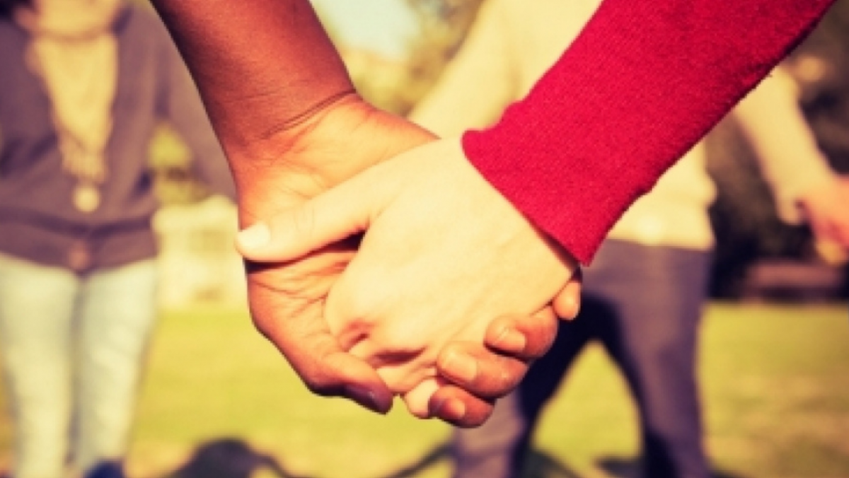 Close up of people holding hands, one with brown skin and one with light skin