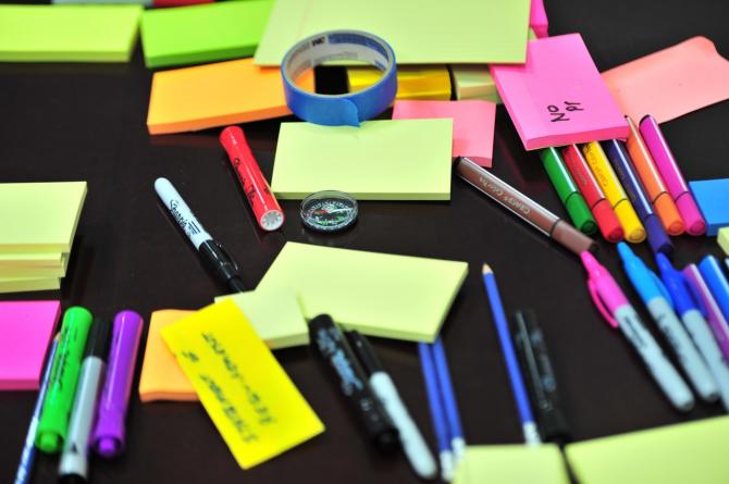 desk strewn with markers, sticky notes, pens, and other art supplies