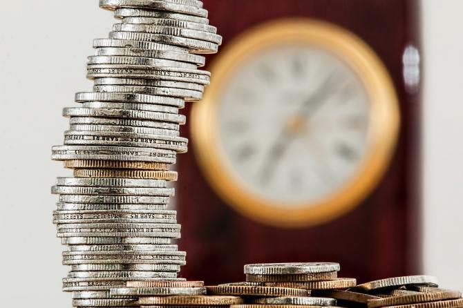 stack of silver and gold coins with out-of-focus clock in the background