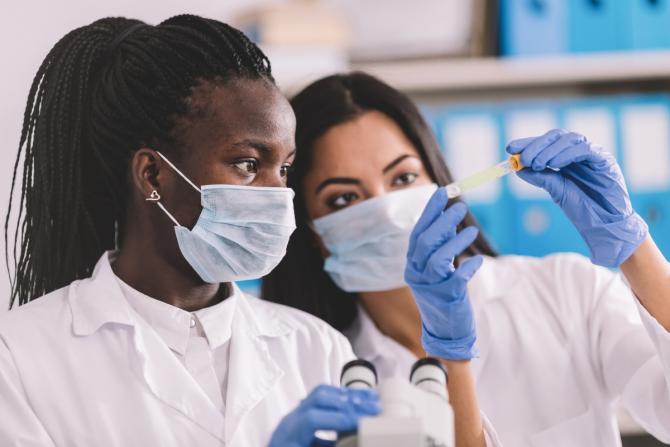 two masked women scientists in laboratory with microscope and sample tube