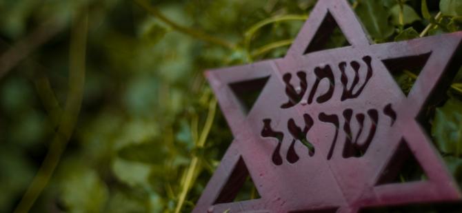Bronze star of David with "Shema Yisrael" / "Hear O Israel" engraved into its solid center, hanging against a background of greenery