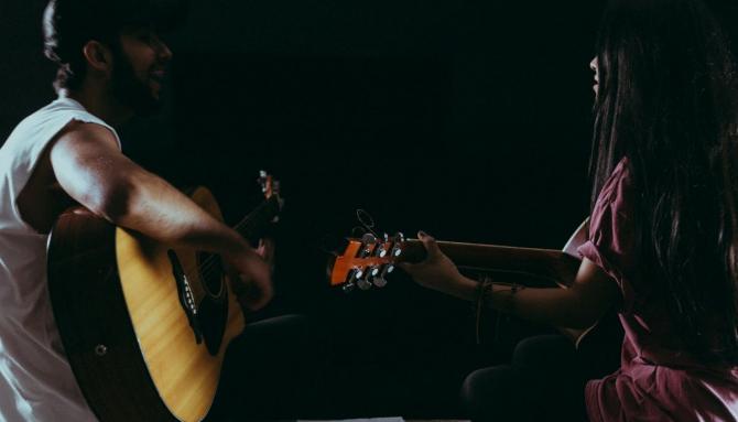 profile view of a man and a woman playing guitar while facing one another