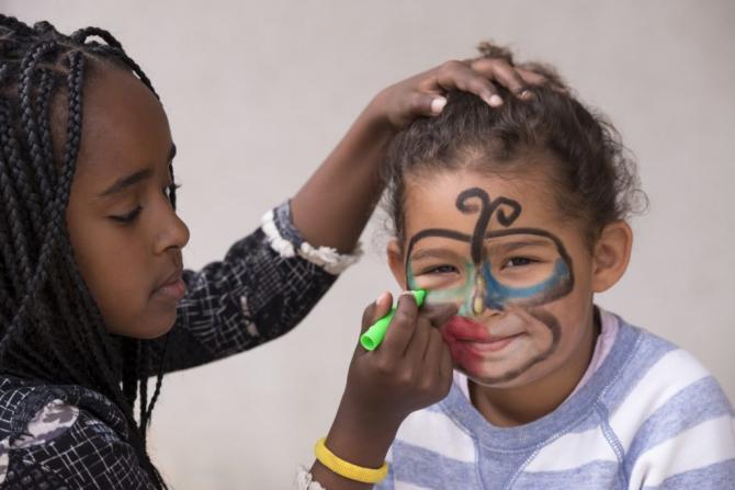 Smiling girl having face paint applied by a friend