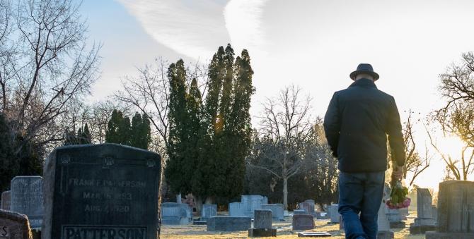 man standing in graveyard with back toward the viewer