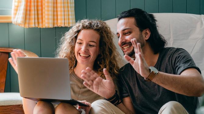 Man and woman sitting on couch smiling and gesturing at laptop screen