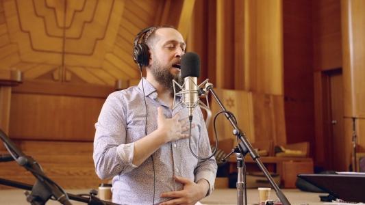 Rabbi Yosef Goldman singing into microphone in front of wooden ark in synagogue