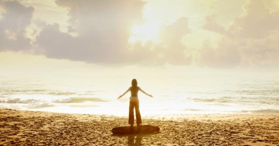 figure on beach standing facing brilliant sky with light reflecting off water