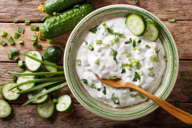 ceramic bowl of yogurt with cut-up cucumbers and scallions