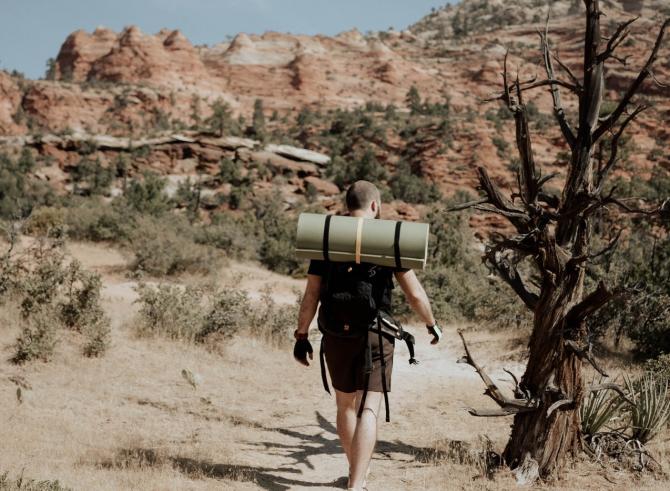 backpacker with bedroll on back walking into desert