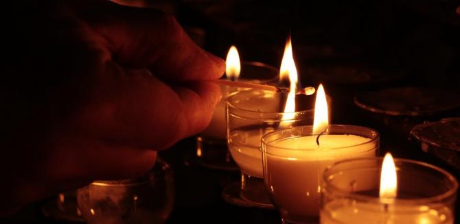 Close-up of a hand lighting a series of memorial candles