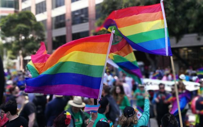 Crowd of people waving rainbow flags at a Pride parade