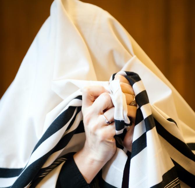 Person covering their head with a white tallit with black stripes