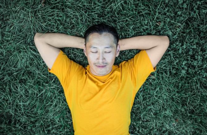 man in yellow shirt sleeping on grass with hands behind his head