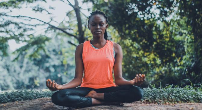 woman of color meditating seated in lotus position in forest