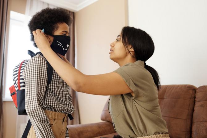 woman putting mask on boy with backpack