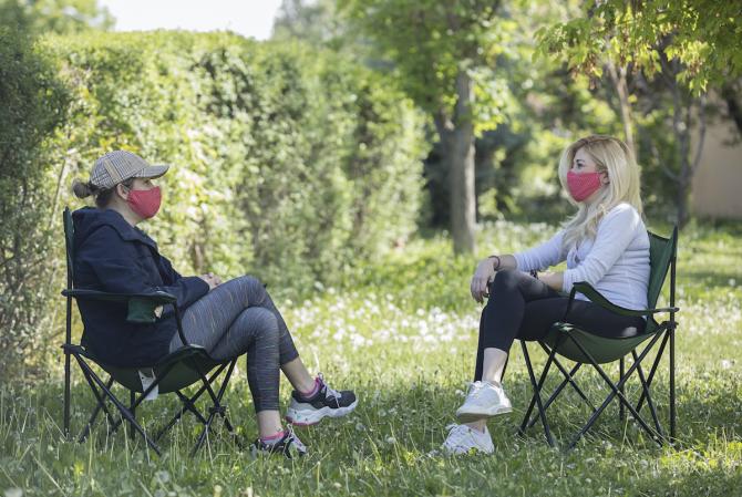 Two people sitting facing one another in lawn chairs, wearing face masks