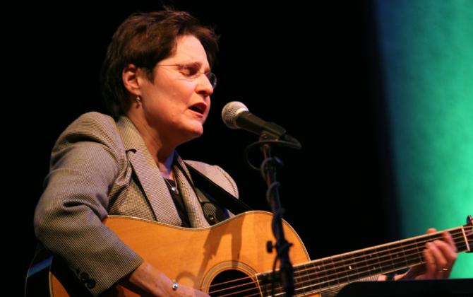 woman with guitar (Debbie Friedman) sings into microphone