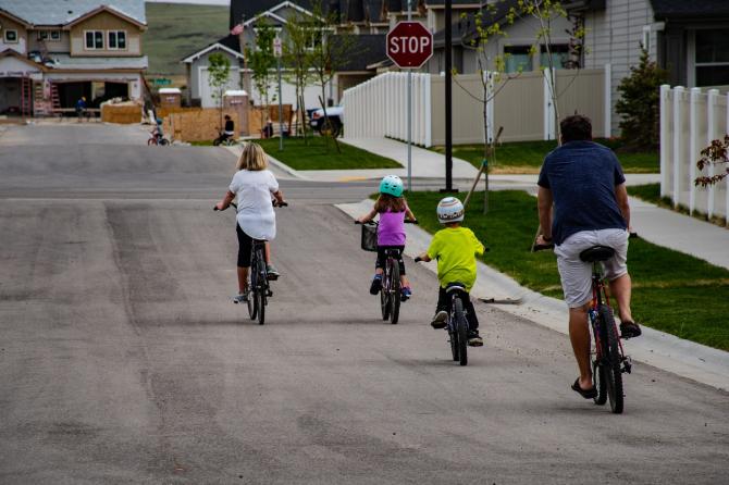 two adult and two children riding bicylcles in the street, viewed from behind