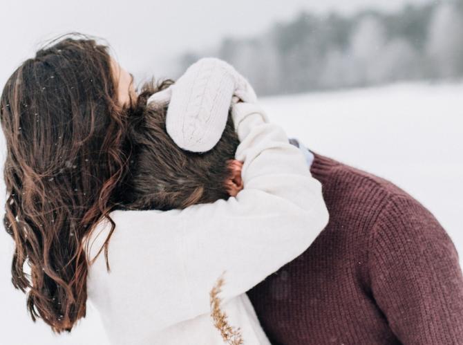 woman in white sweater embracing person in maroon sweater, outdoors in snowy landscape