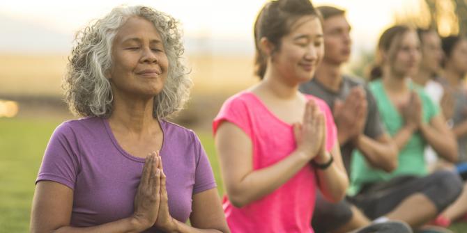 people seated outdoors meditating with eyes closed and hands clasped