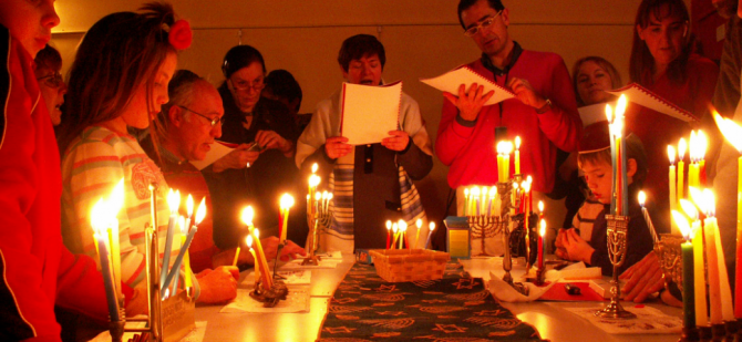 Group gathered around of table of Hanukkah menorahs