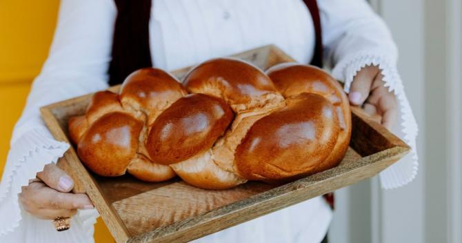 person in white holding wooden tray with large challah