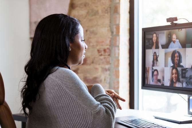 woman seated at computer in video call with six other people