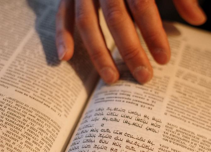 open book with Hebrew and Cyrillic text, and hand resting on the text