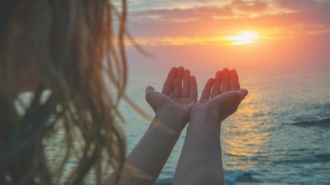 A person holding their hands out towards the sunset over the ocean