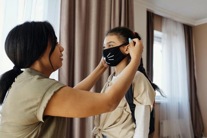 Adult fitting a protective mask on a child's face
