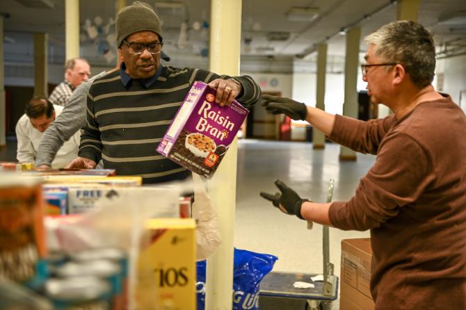 Man checking out at grocery story wearing gloves, holding a box of raisin bran