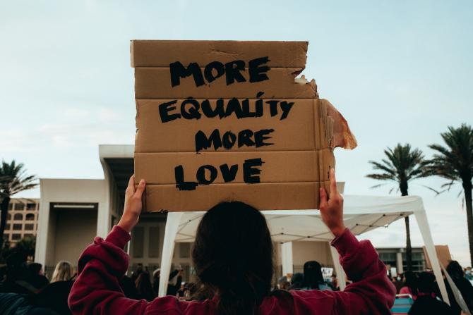 Protester holding hand-lettered sign reading "More equality, more love"