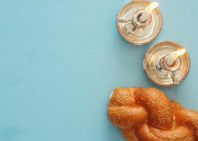 Looking down on wooden table holding challah and burning Shabbat candles