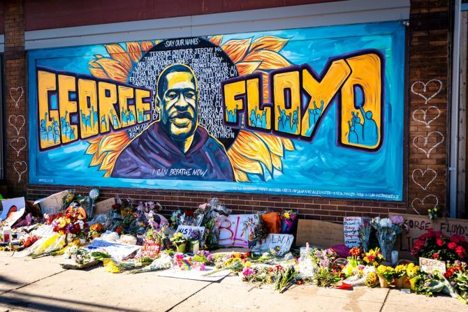 Mural of George Floyd painted on brick wall with memorial items at its feet