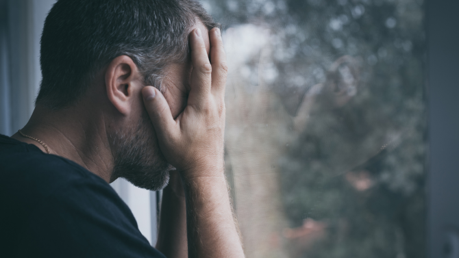 Man at a window covering his face