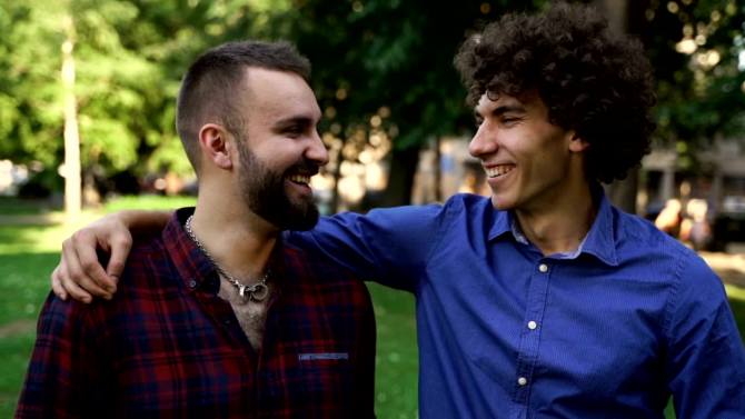 Two men in the park, man in blue shirt with his arm around man in plaid shirt