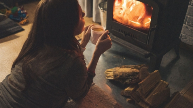 A woman drinking coffee by a wood fireplace