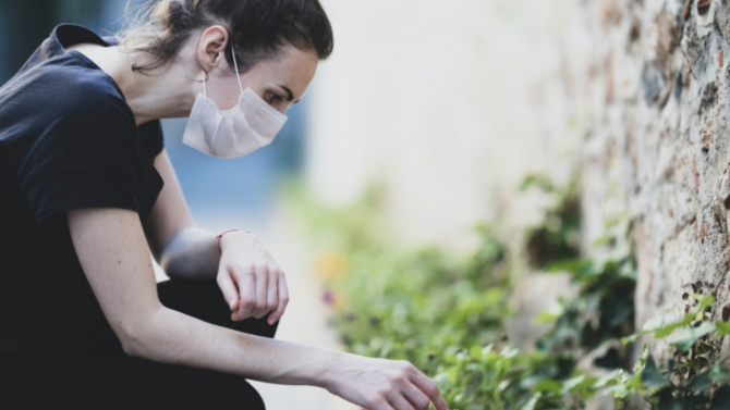 Woman in a surgical mask kneeling by a wall outside