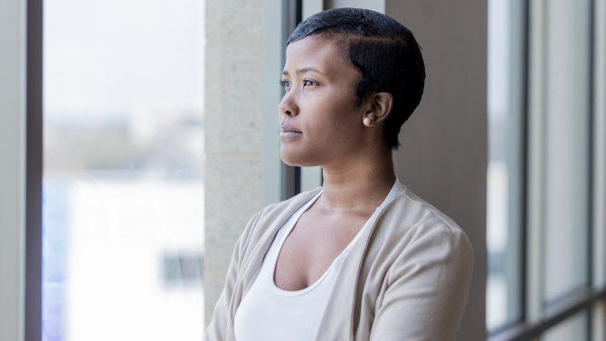 A Black woman with short hair looking serious and staring out a window