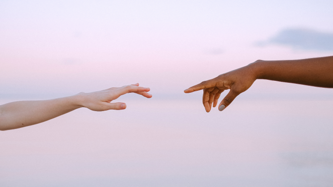 Black hand and white hand nearly touching against a sky backdrop