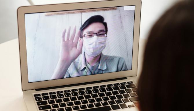 laptop screen showing masked person raising hand in greeting