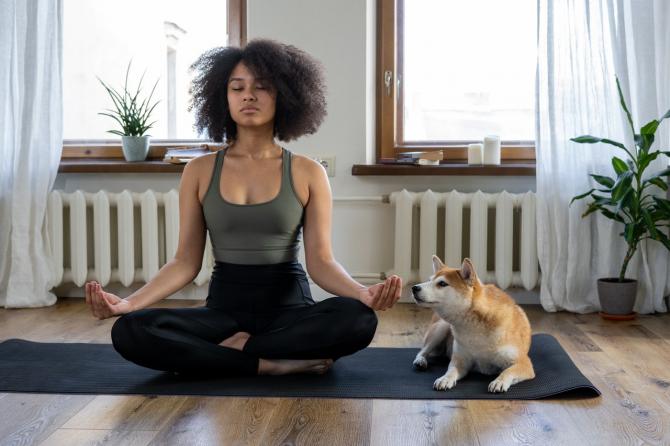 Person sitting in the Yoga Lotus position alongside a dog