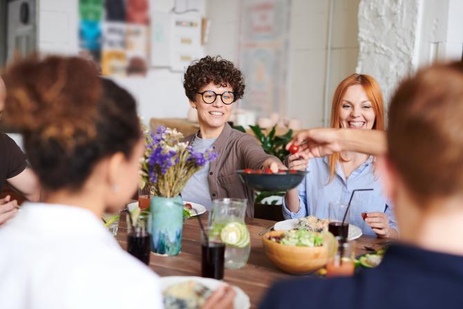 Woman passing salad across a crowded dinner table