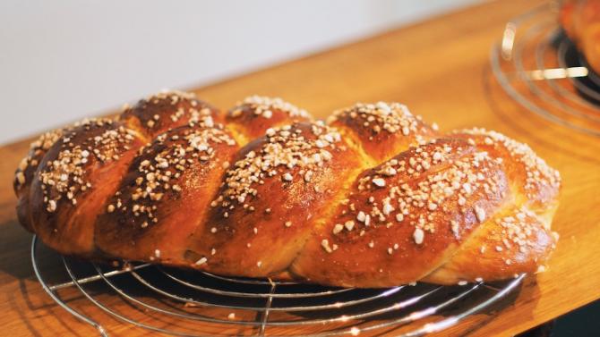 loaf of fresh-baked challah with sesame seeds on a countertop wire cooling rack