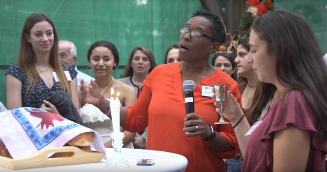 College students gathered around Shabbat candles and challah, with Rabbi Sandra Lawson at the center leading prayers