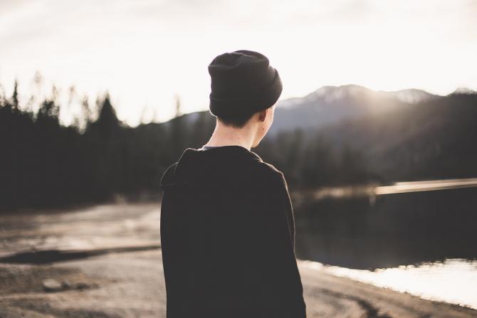 Figure viewed from the back dressed in black, looking out over a lake and mountains