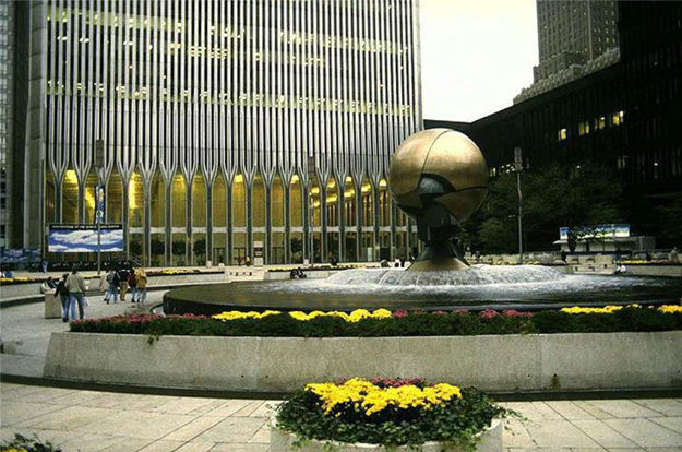 Outdoor view of World Trade Center plaza with flowerbeds and fountain in the foreground and tall buildings in the background