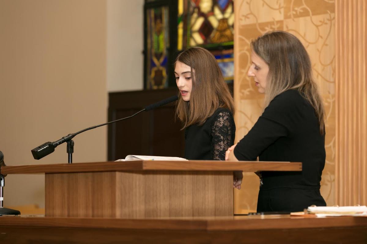 Girl reading from a prayer book on the bimah at synagogue